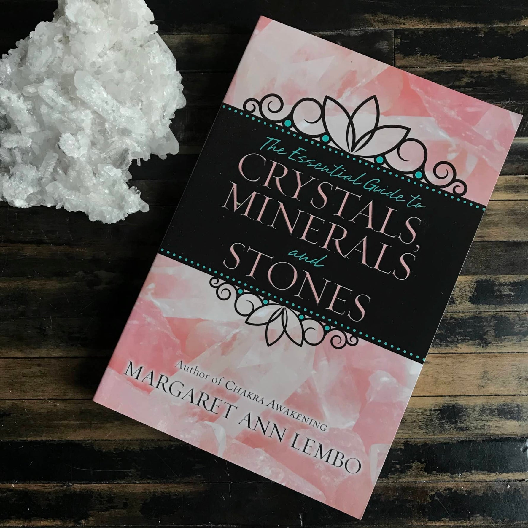 Book titled 'The Essential Guide to Crystals, Minerals and Stones' by Margaret Ann Lembo on a wooden surface with crystals.