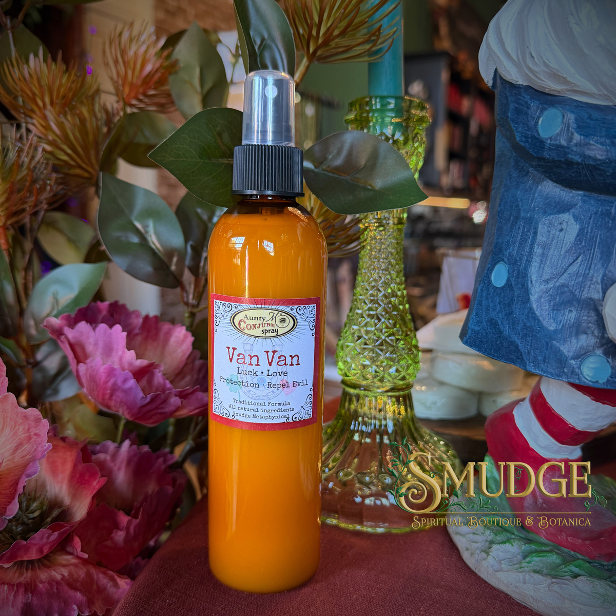 An orange-colored spray bottle labeled 'Van Van' by Smudge & Co, styled with flowers and a green glass vase in a decorative setting.