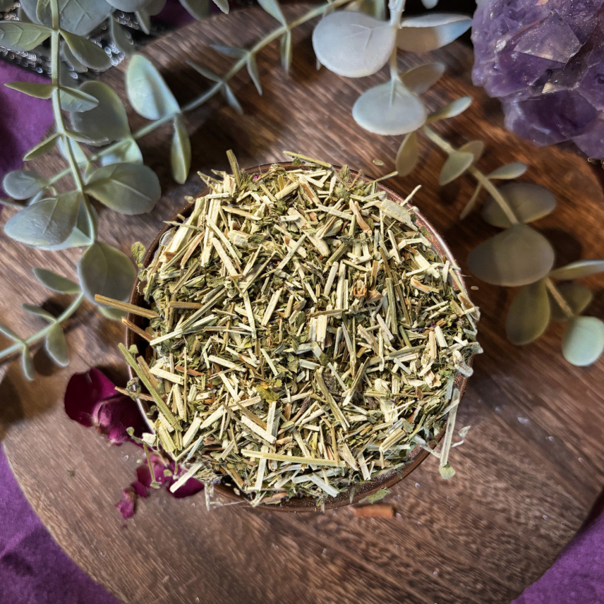 Dried herbs in a wooden bowl with eucalyptus leaves and a purple stone on a dark background
