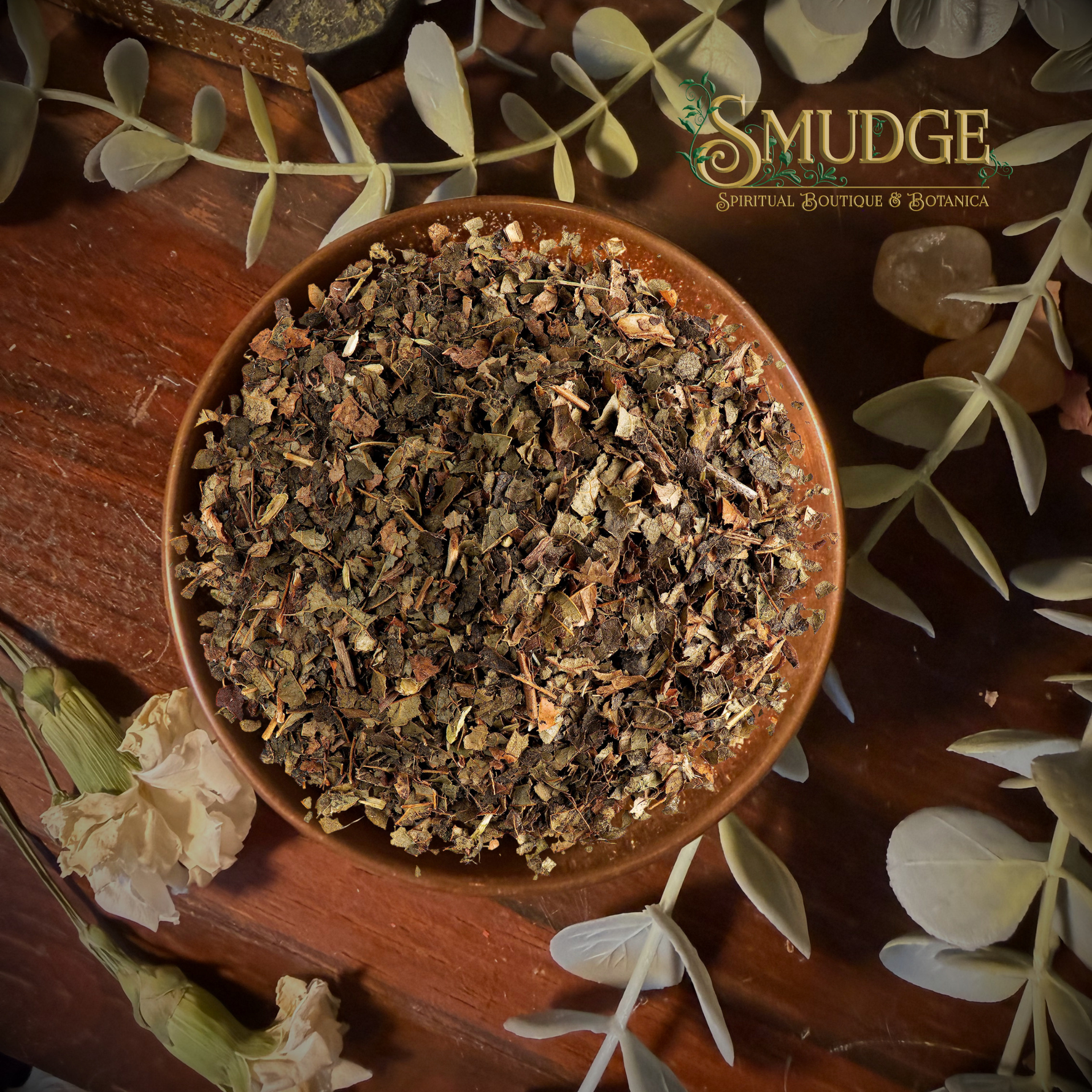 A top-down view of a brown ceramic bowl filled with dried botanical herb mixture, surrounded by eucalyptus leaves, crystals, and flowers on a wooden surface. The 'Smudge Spiritual Boutique & Botanica' logo is visible in the top right corner.